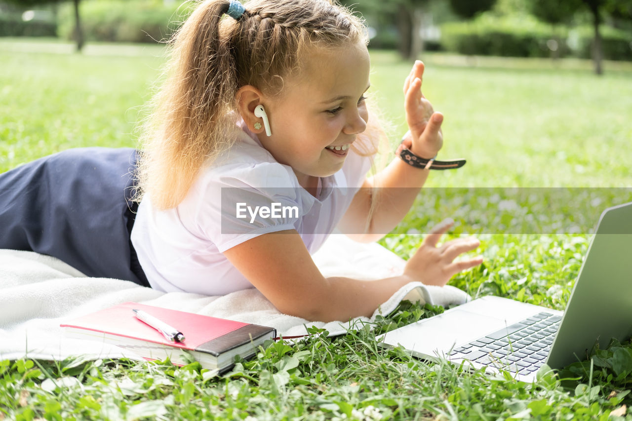 young woman using laptop while sitting on field