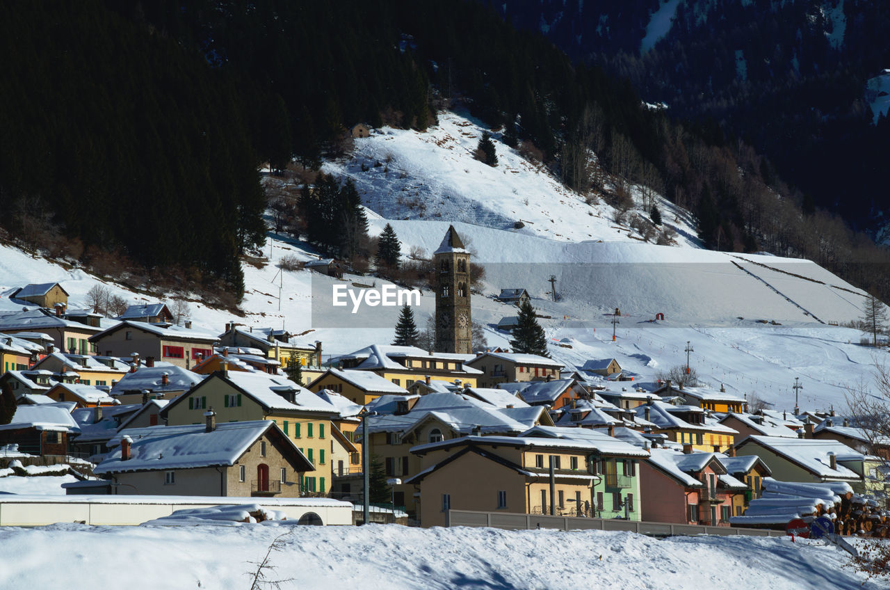 HIGH ANGLE VIEW OF HOUSES ON SNOW COVERED FIELD AGAINST MOUNTAIN