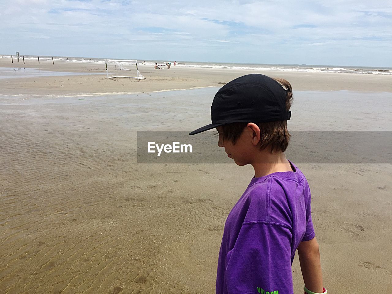 Side view of boy wearing cap while standing on sand at beach