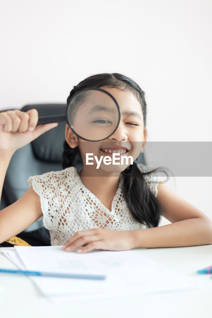 Portrait of smiling girl holding magnifying glass on table