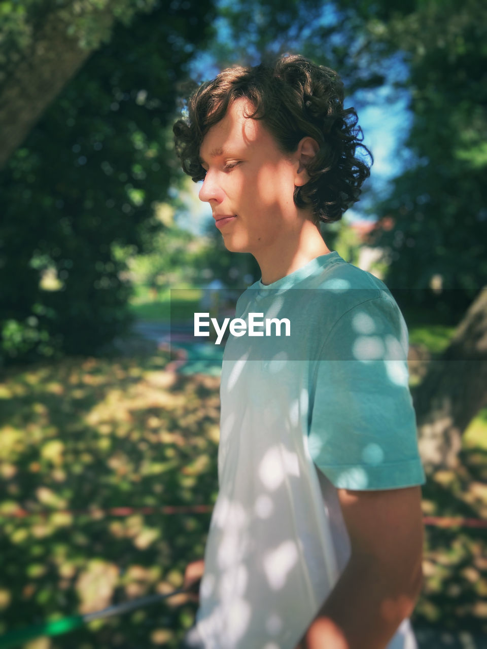 Side view of young  teenage boy standing against trees