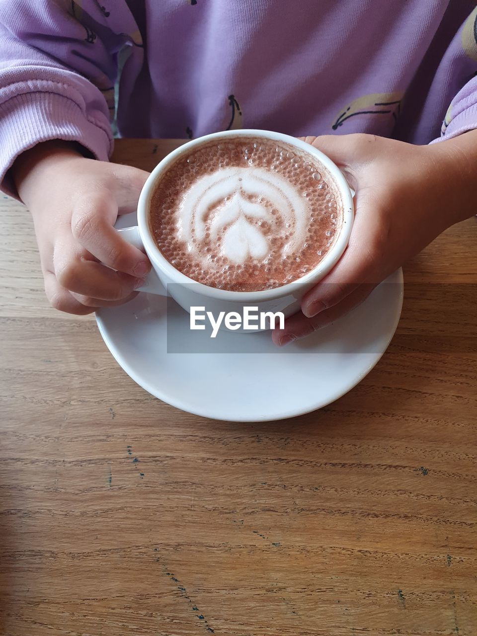food and drink, one person, drink, coffee, refreshment, cup, mug, coffee cup, hand, holding, women, adult, indoors, table, hot drink, directly above, frothy drink, crockery, cappuccino, food, wood, lifestyles, high angle view, latte, saucer, freshness, froth art, kitchen utensil, midsection, eating utensil, spoon