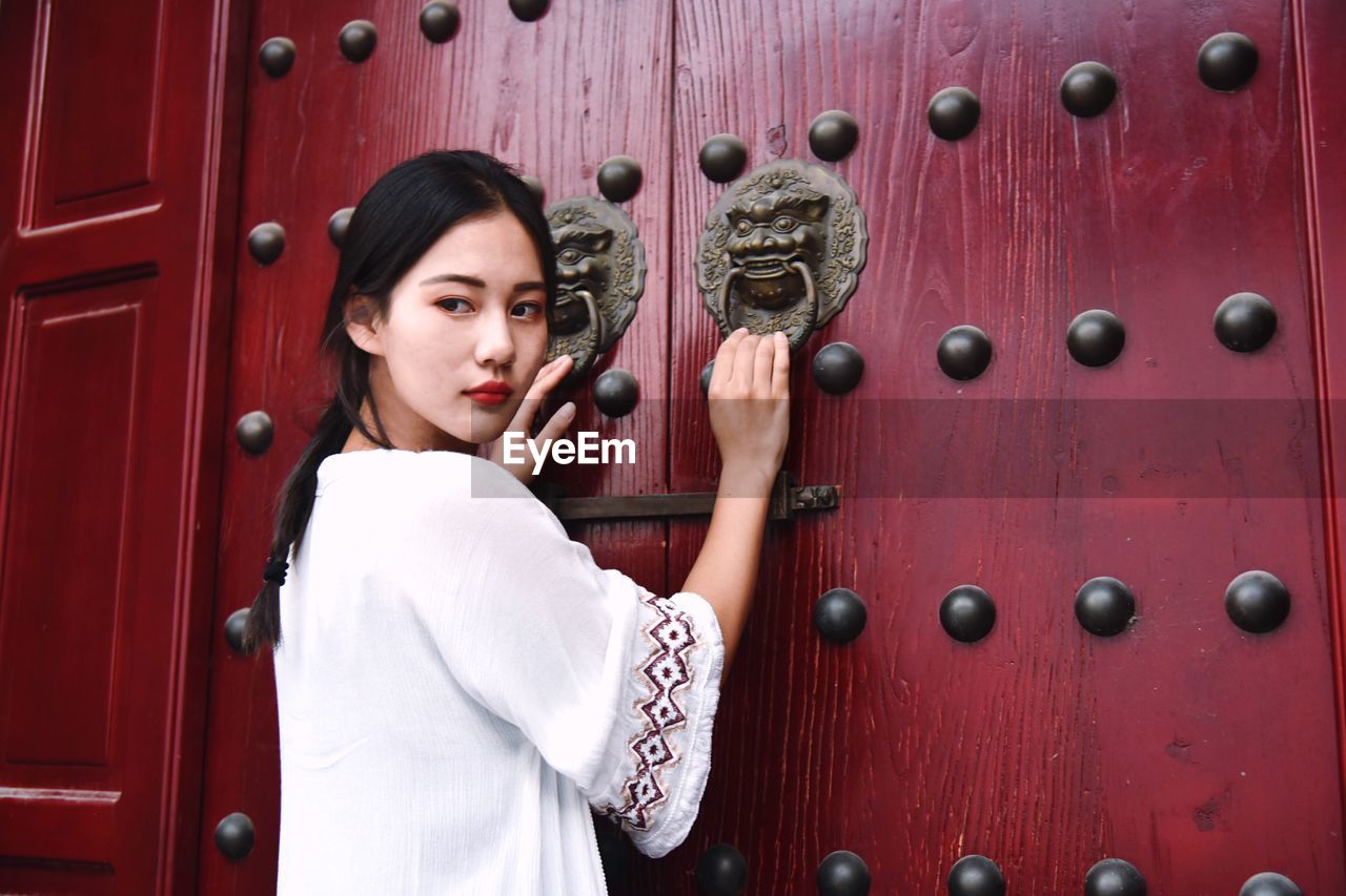 Young woman holding door knockers of maroon wooden gate
