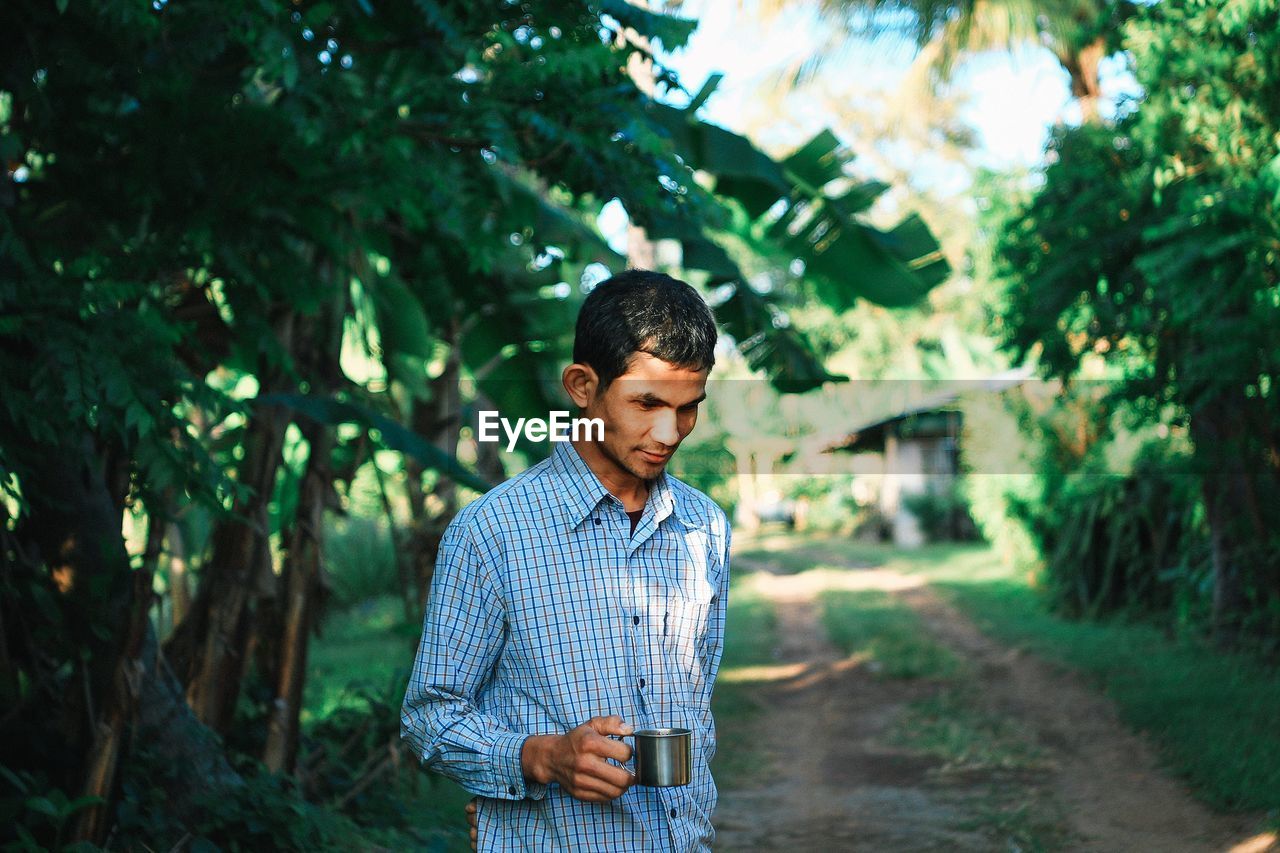 YOUNG MAN STANDING BY TREE AGAINST PLANTS