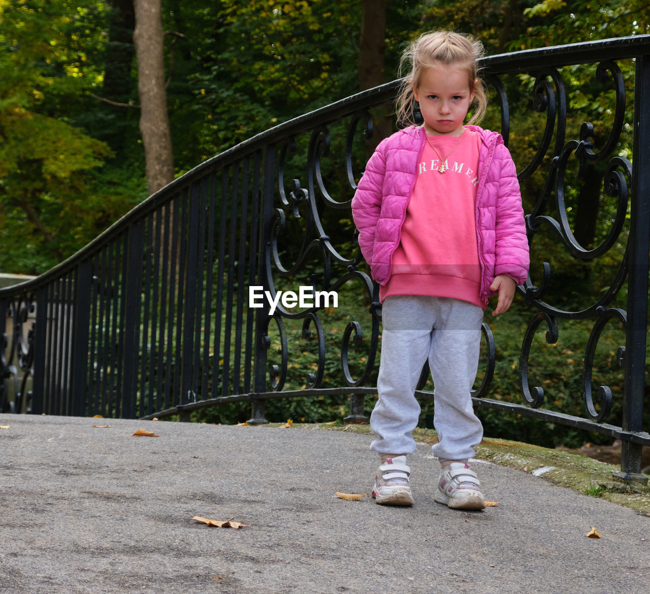 childhood, child, one person, full length, spring, casual clothing, female, standing, front view, leisure activity, women, blond hair, day, tree, lifestyles, portrait, nature, plant, railing, person, innocence, outdoors, architecture, looking at camera, pink, emotion, cute, smiling, toddler, clothing, looking, fence