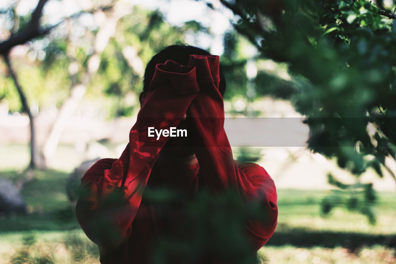 Man covering face while standing in forest