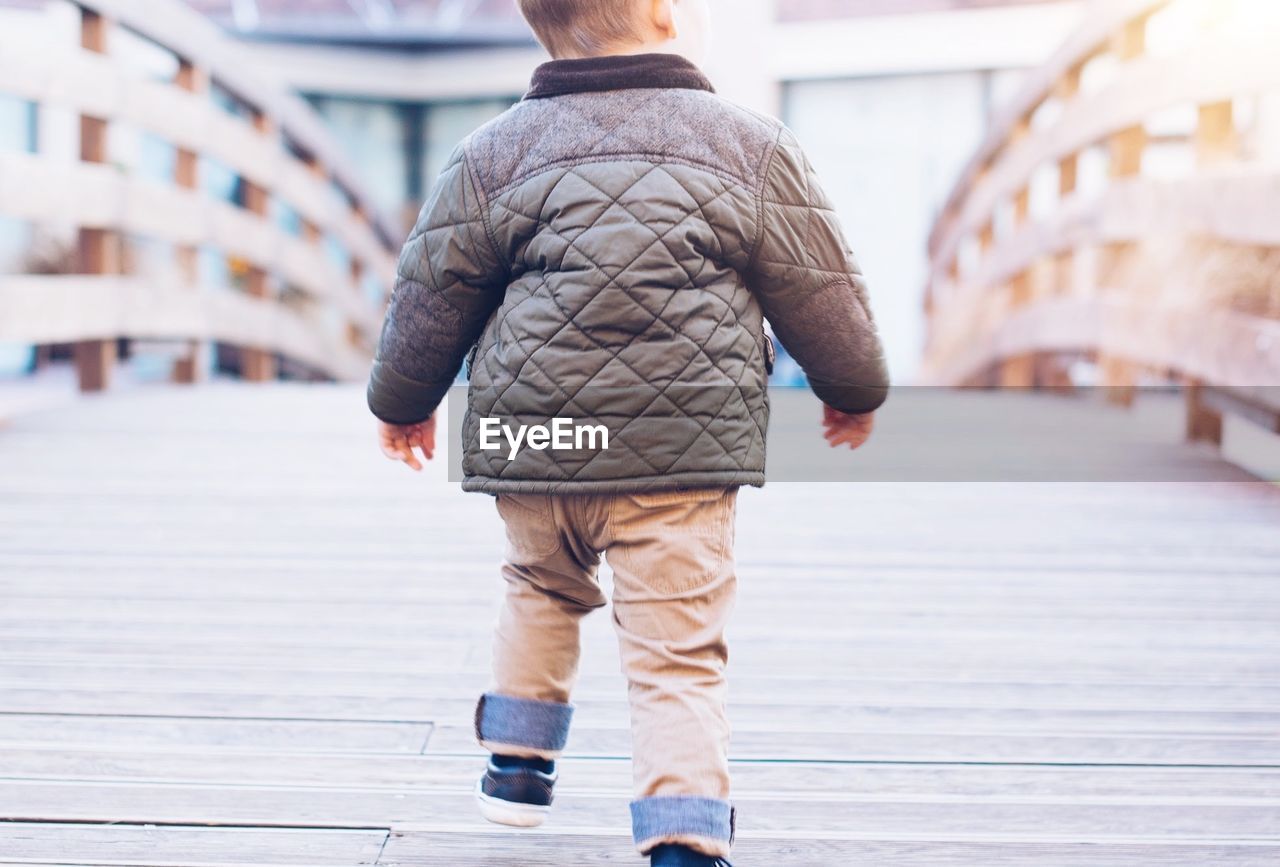 Rear view of boy walking on footbridge in city