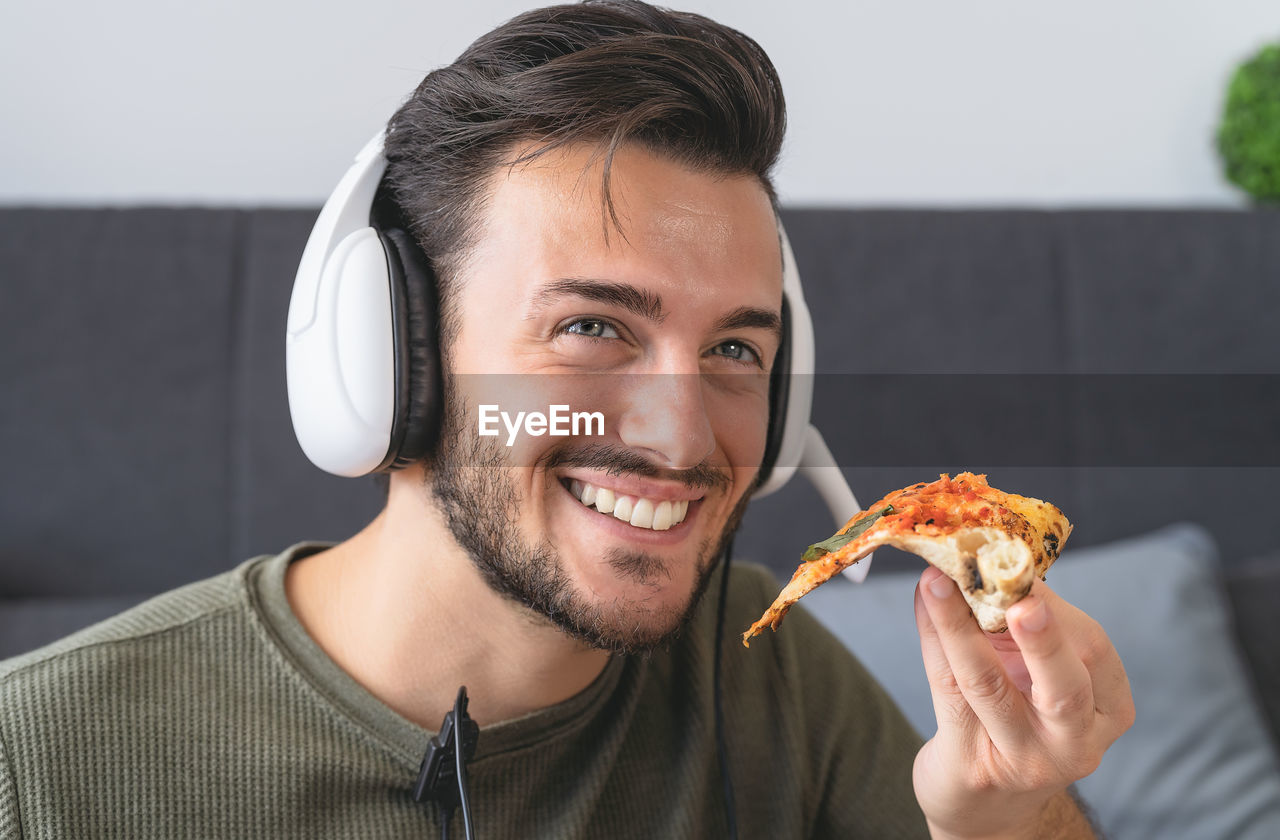 Young man eating delivery pizza at home - happy guy having meal while video calling with family