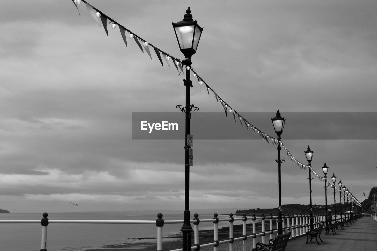 Low angle view of street lights by pier against sky