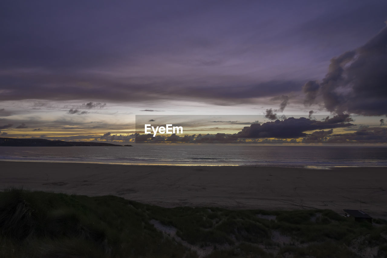 Scenic view of beach against cloudy sky during sunset