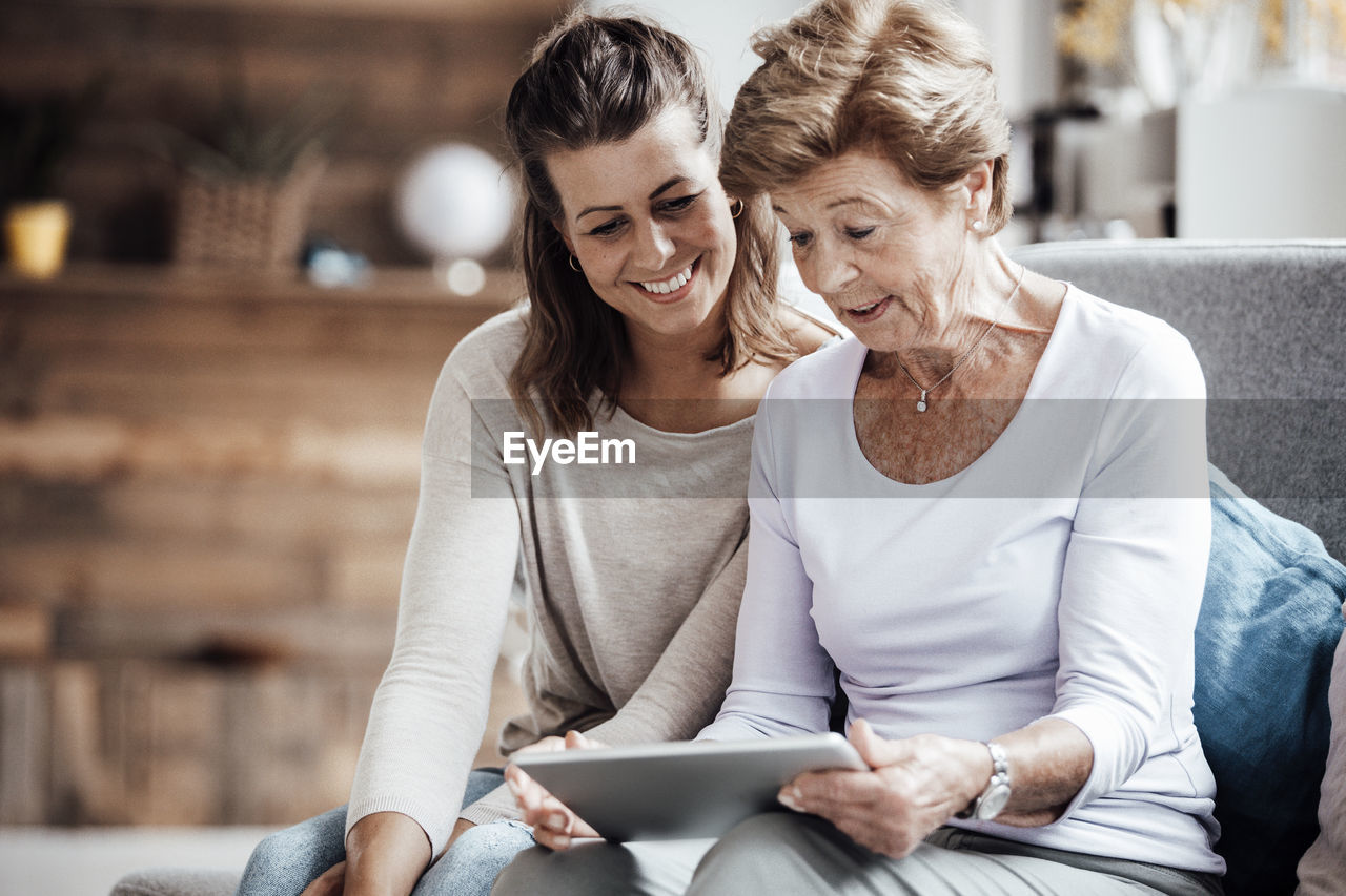 Surprised senior woman using digital tablet by granddaughter at home