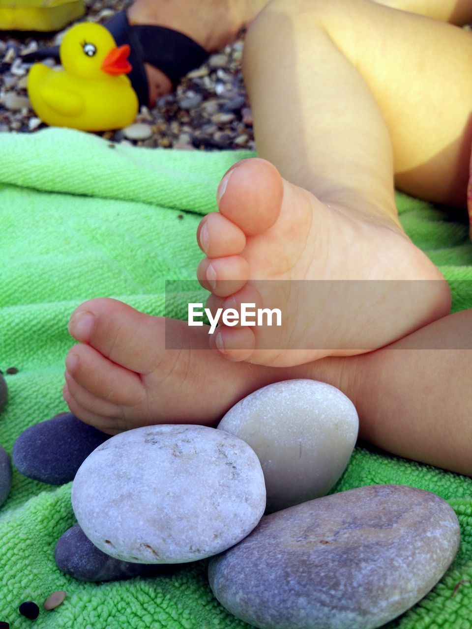 Low section of baby with pebbles on towel at beach