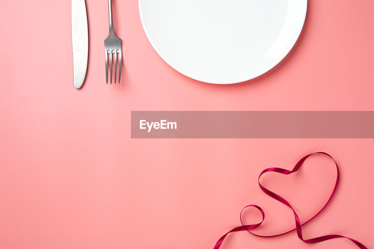 Directly above shot of empty plate with cutlery and ribbon over colored background