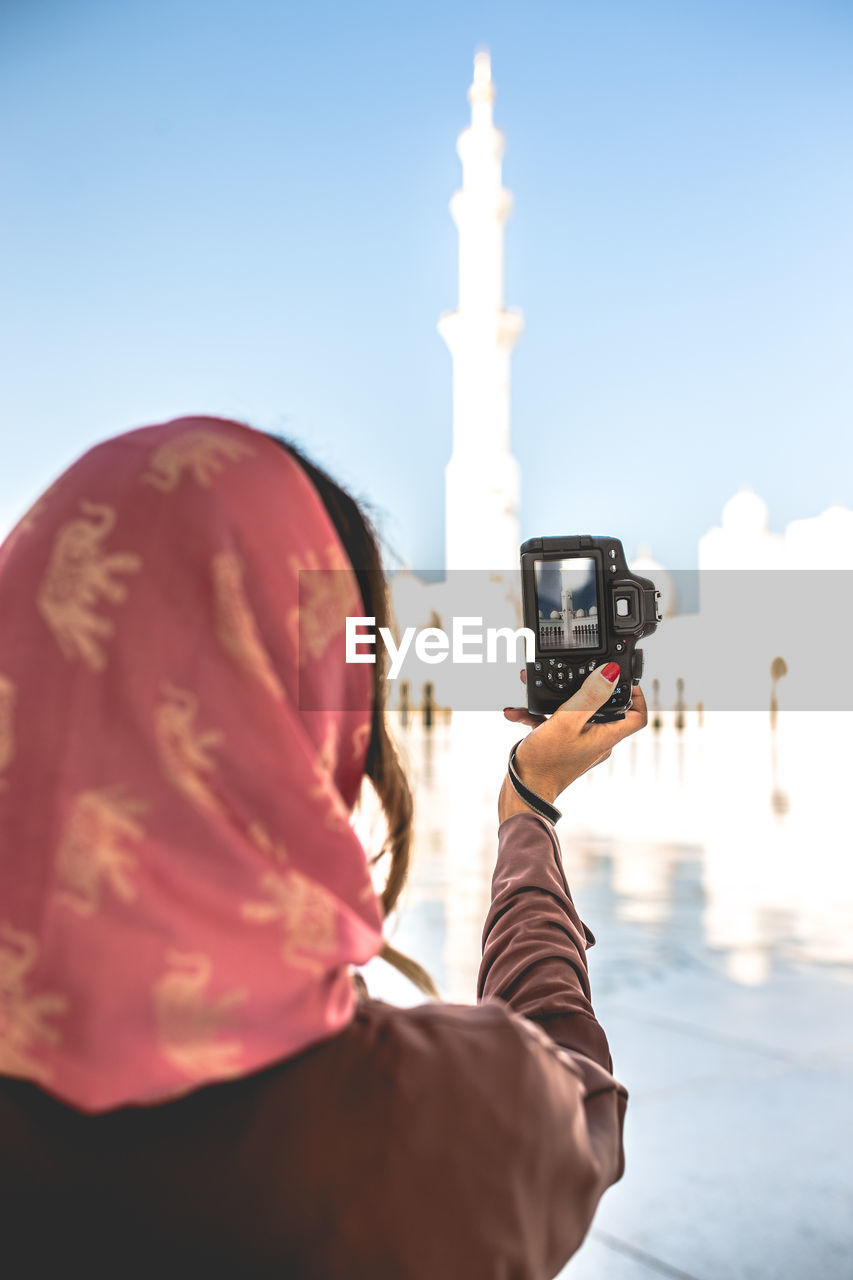 Rear view of woman photographing mosque with camera