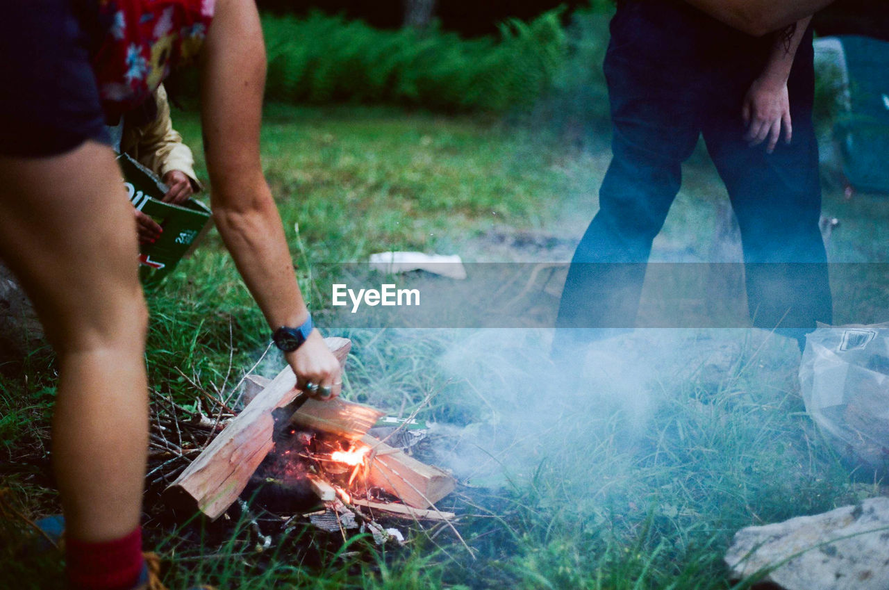 Friends making campfire on grassy field