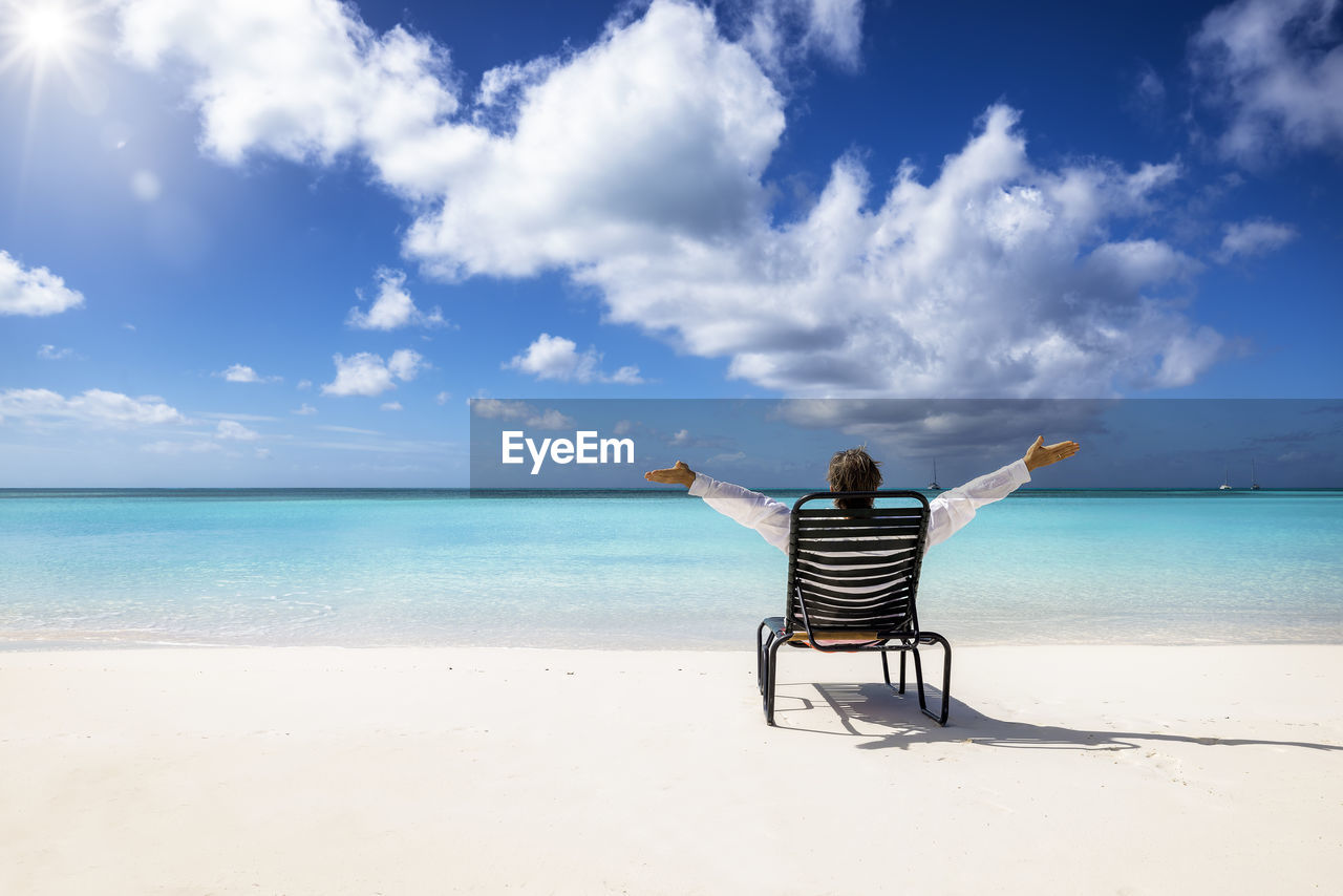 Rear view of man sitting on chair at beach