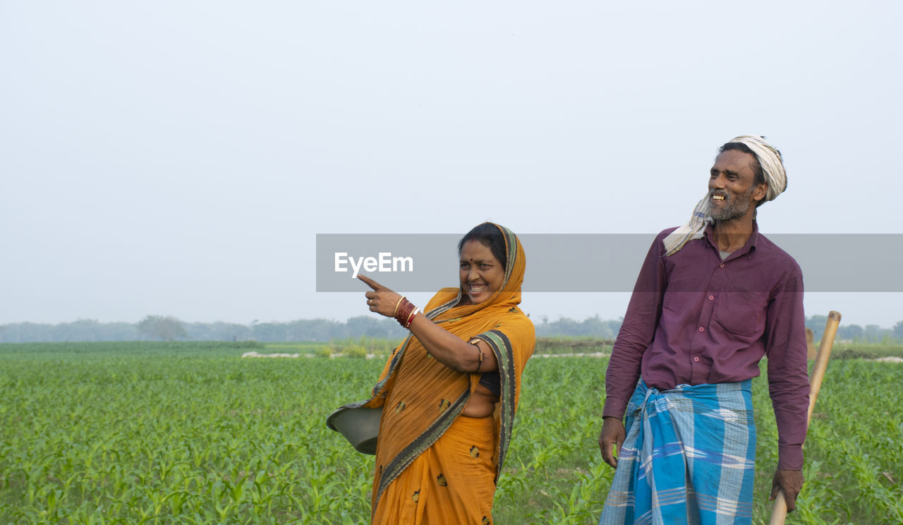 YOUNG COUPLE STANDING ON FIELD AGAINST SKY