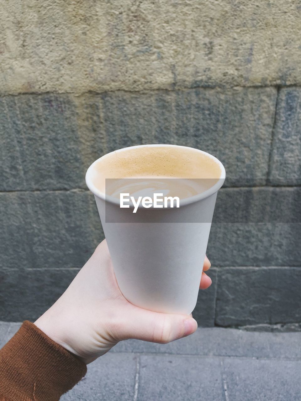 Cropped hand of woman holding coffee cup against wall