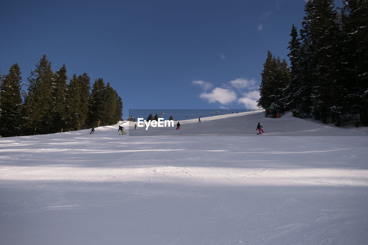 People skiing on snow covered field against sky