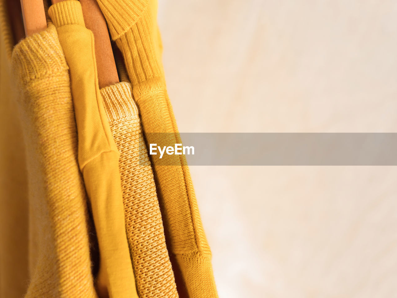 Yellow illuminated color winter sweaters on wooden hangers. trendy fashion autumn warm clothes 