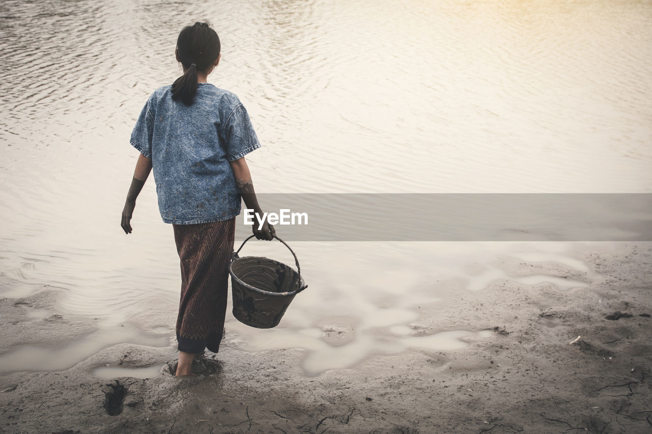 Rear view of girl holding bucket by pond