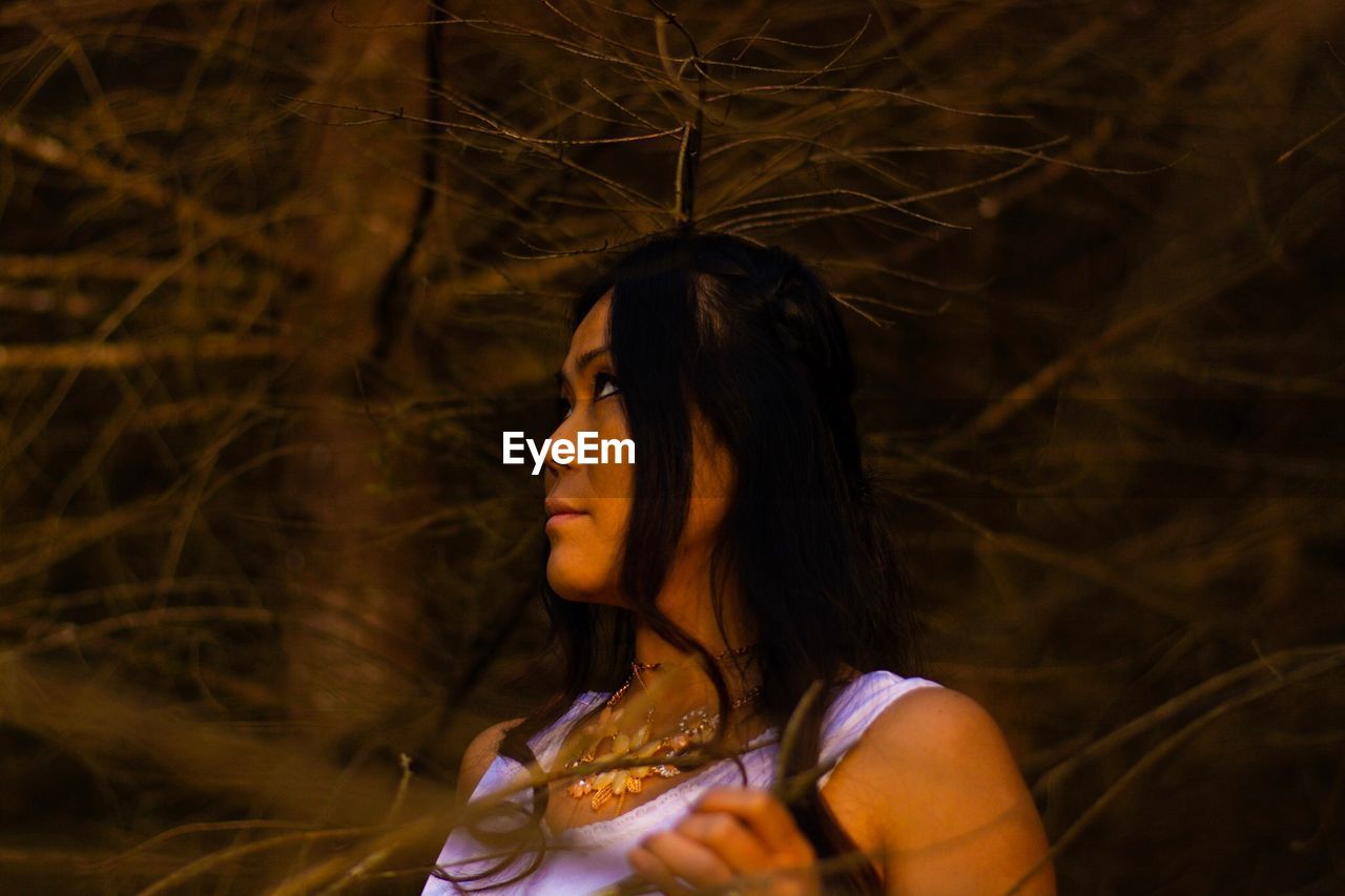 Young woman looking away against trees at night