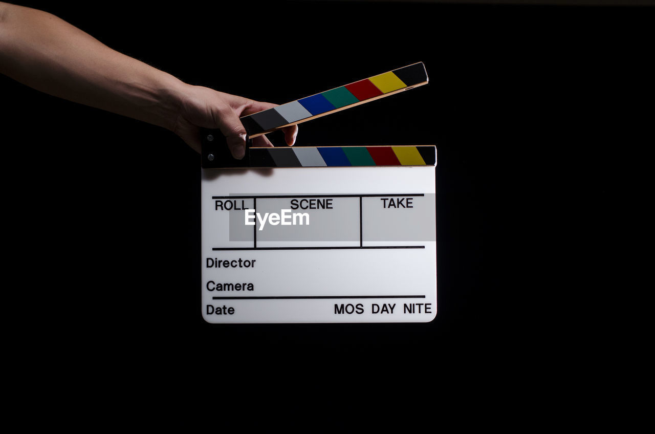 Cropped hand holding film slate against black background