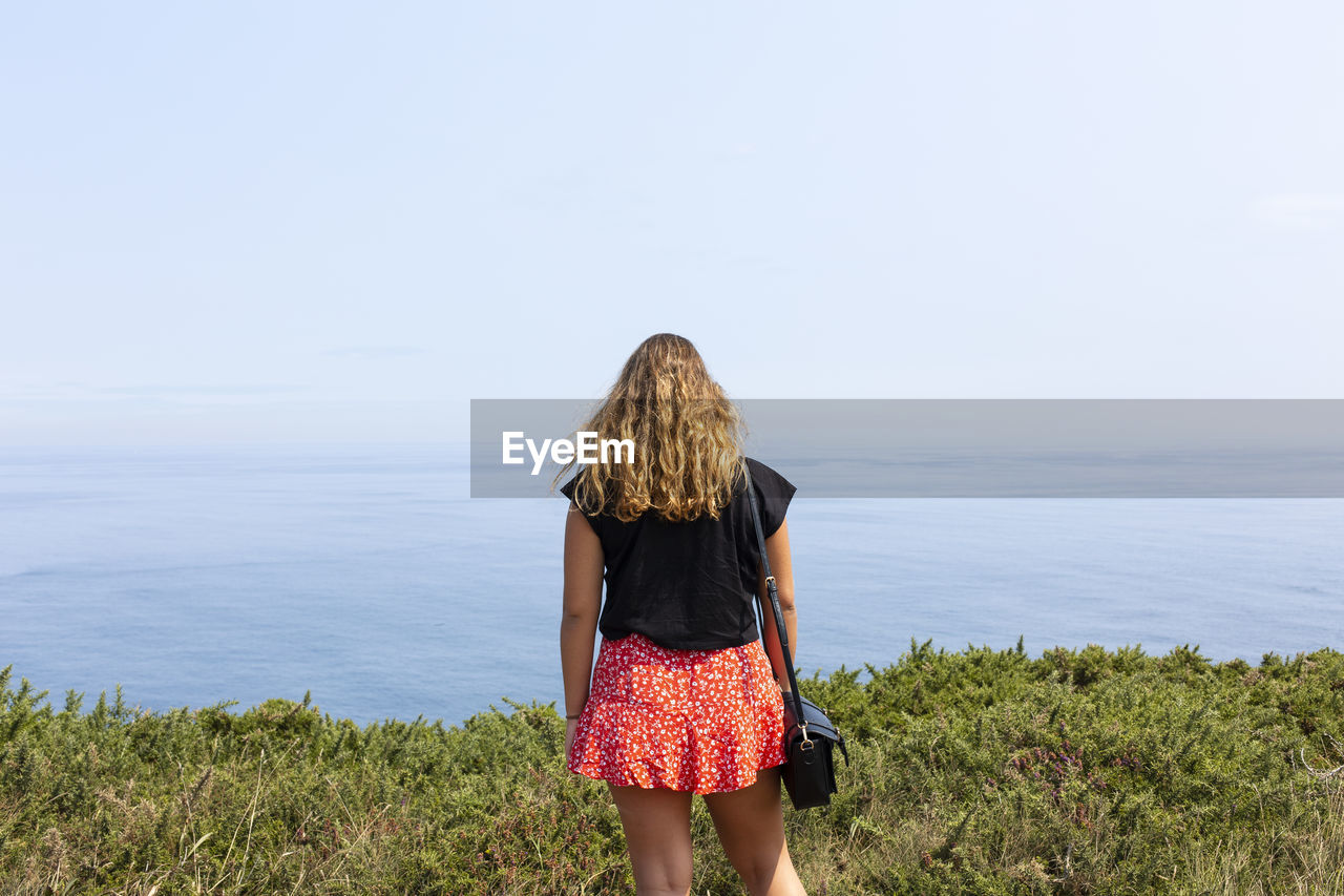 REAR VIEW OF WOMAN STANDING BY SEA