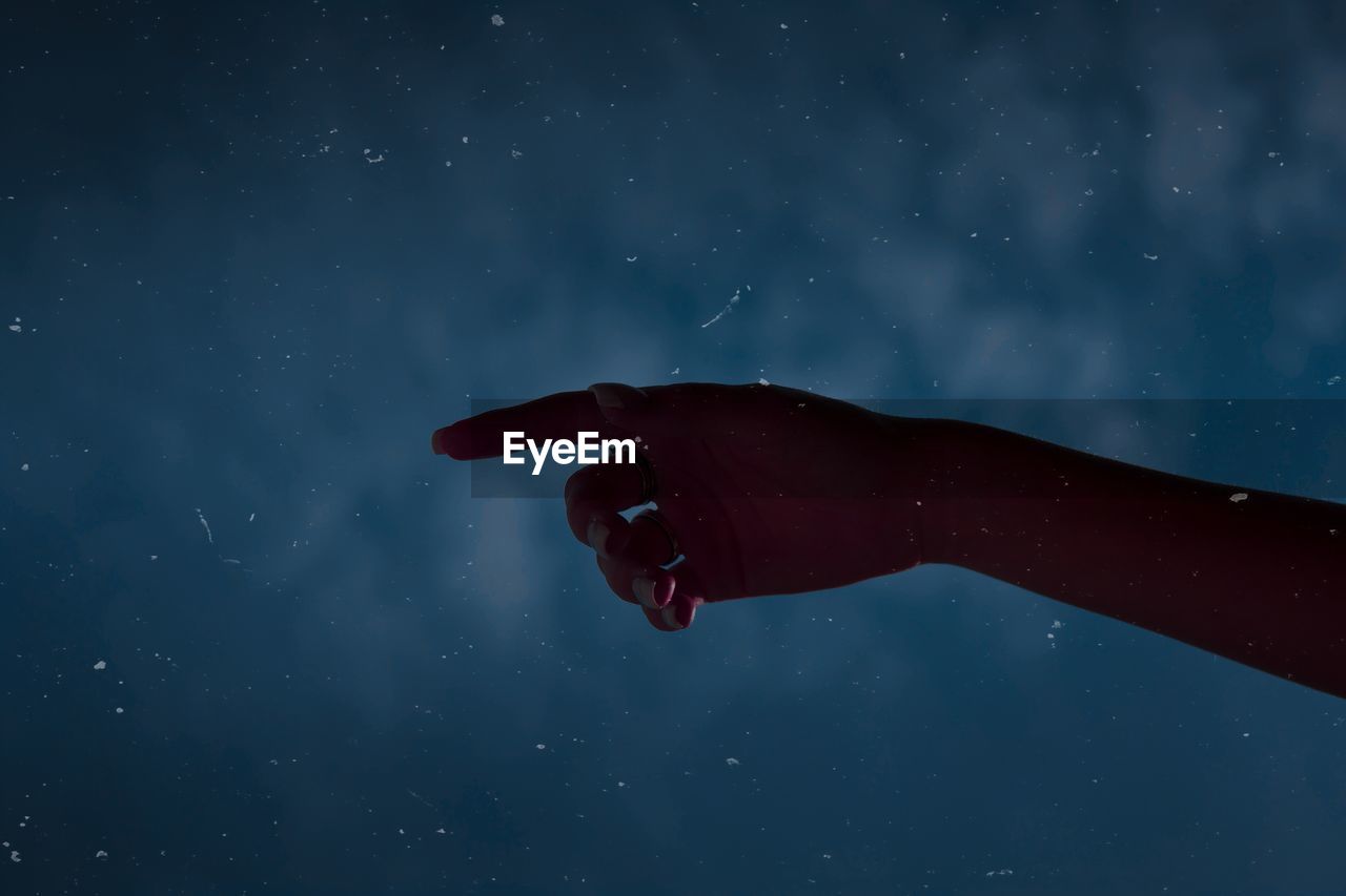 Cropped hand of woman gesturing against sky at night