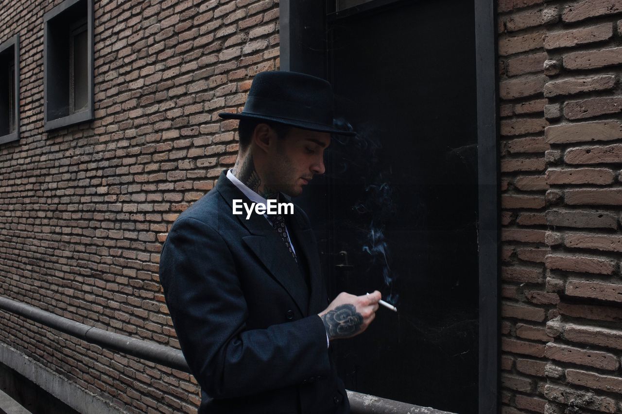 Man smoking cigarette against brick wall