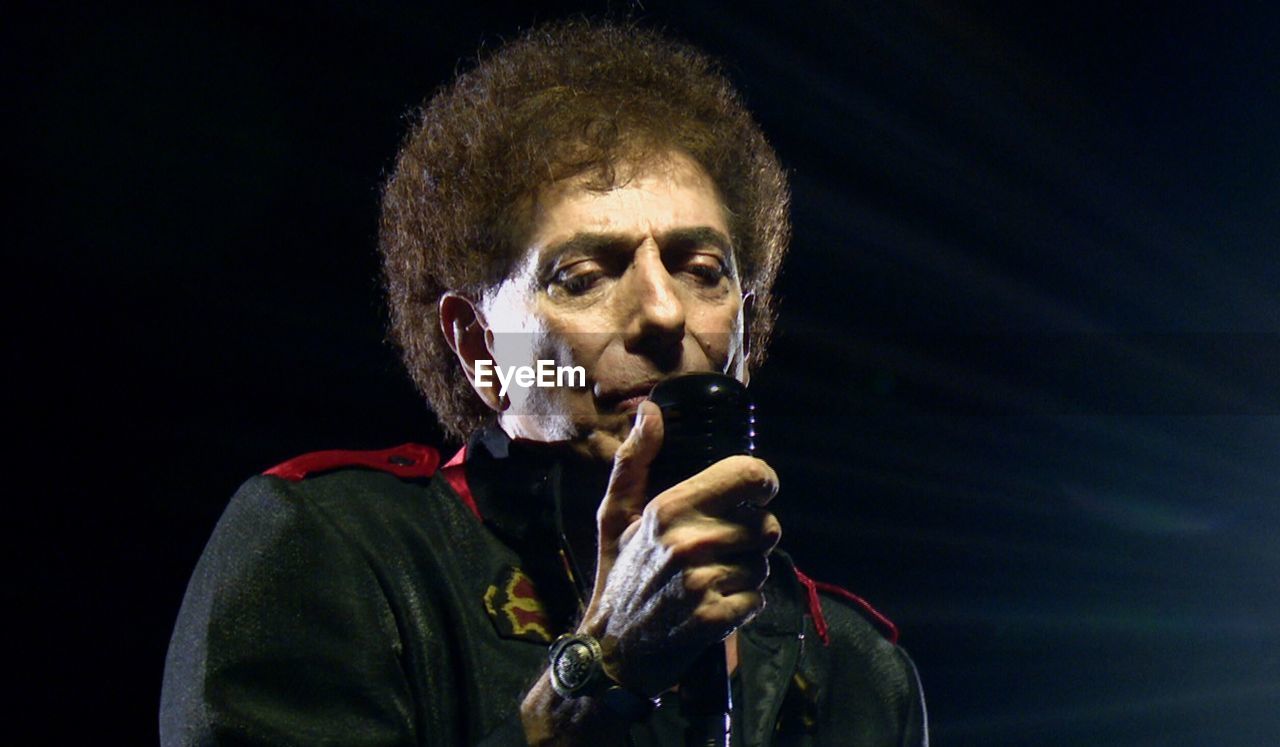 Portrait of man holding microphone over black background