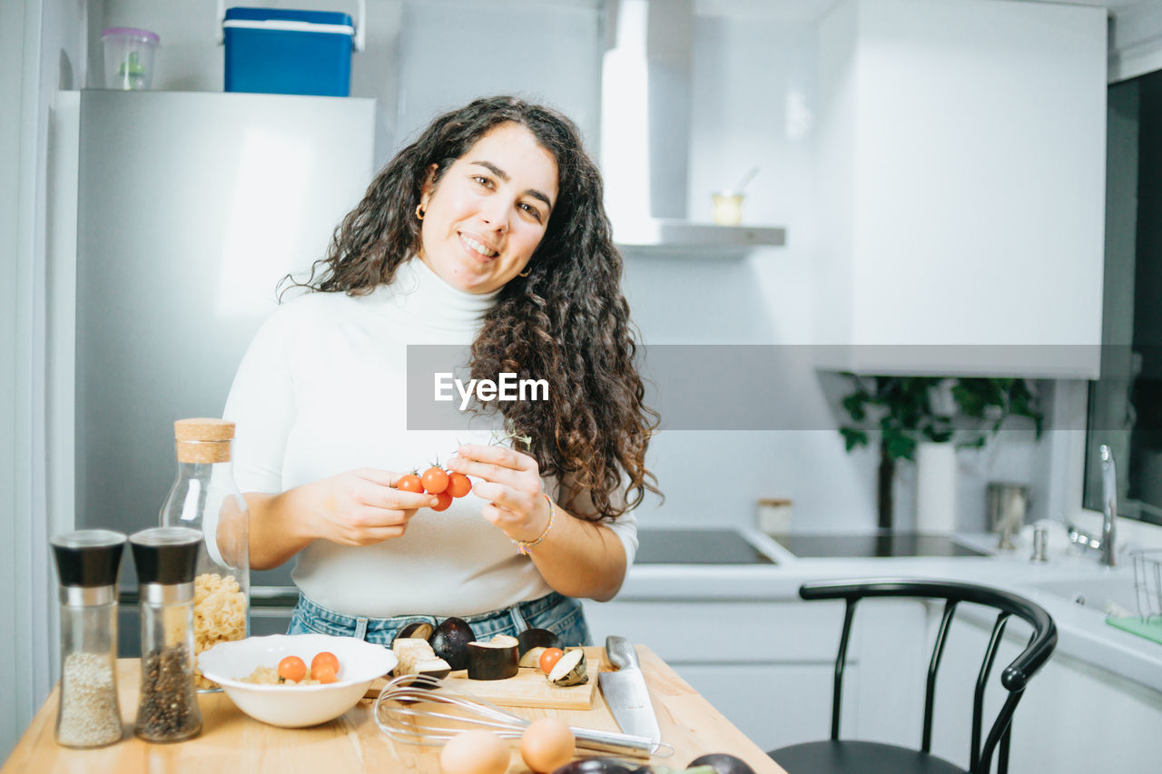 Portrait of smiling woman holding food in kitchen