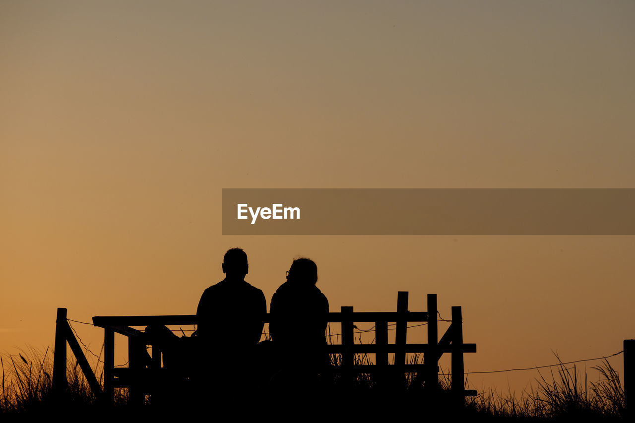 Silhouette couple sitting against orange sky