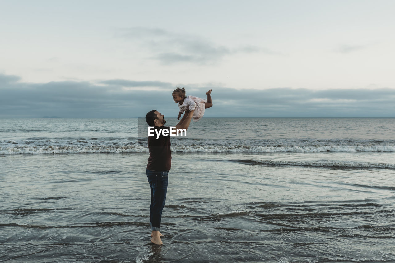 Dad throwing his daughter in air in the ocean negative space