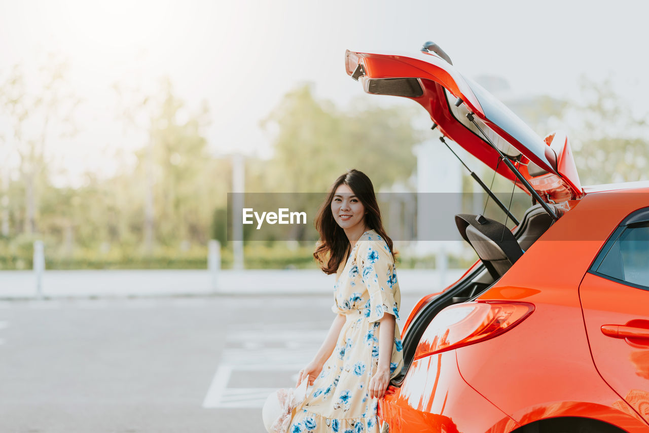 Portrait of smiling beautiful woman sitting on red car trunk