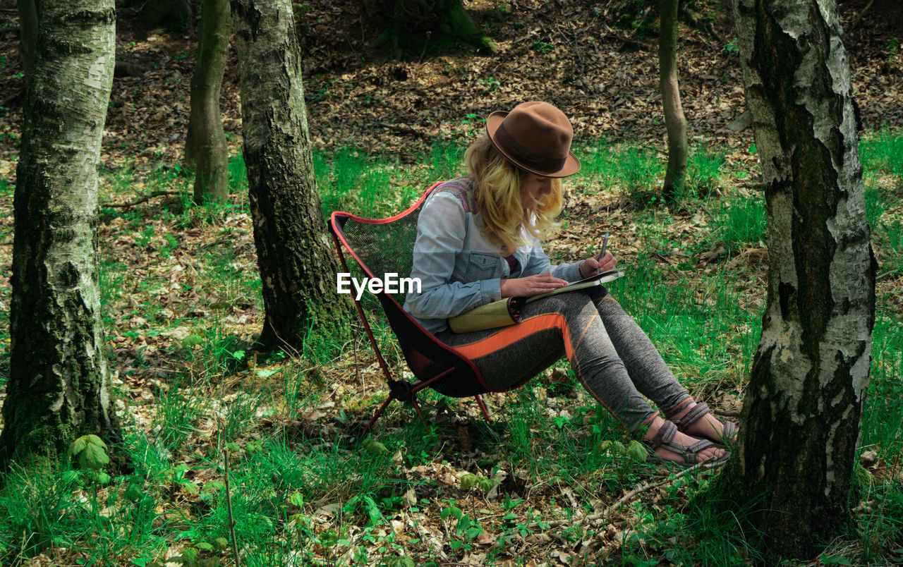 Young woman drawing on book in forest