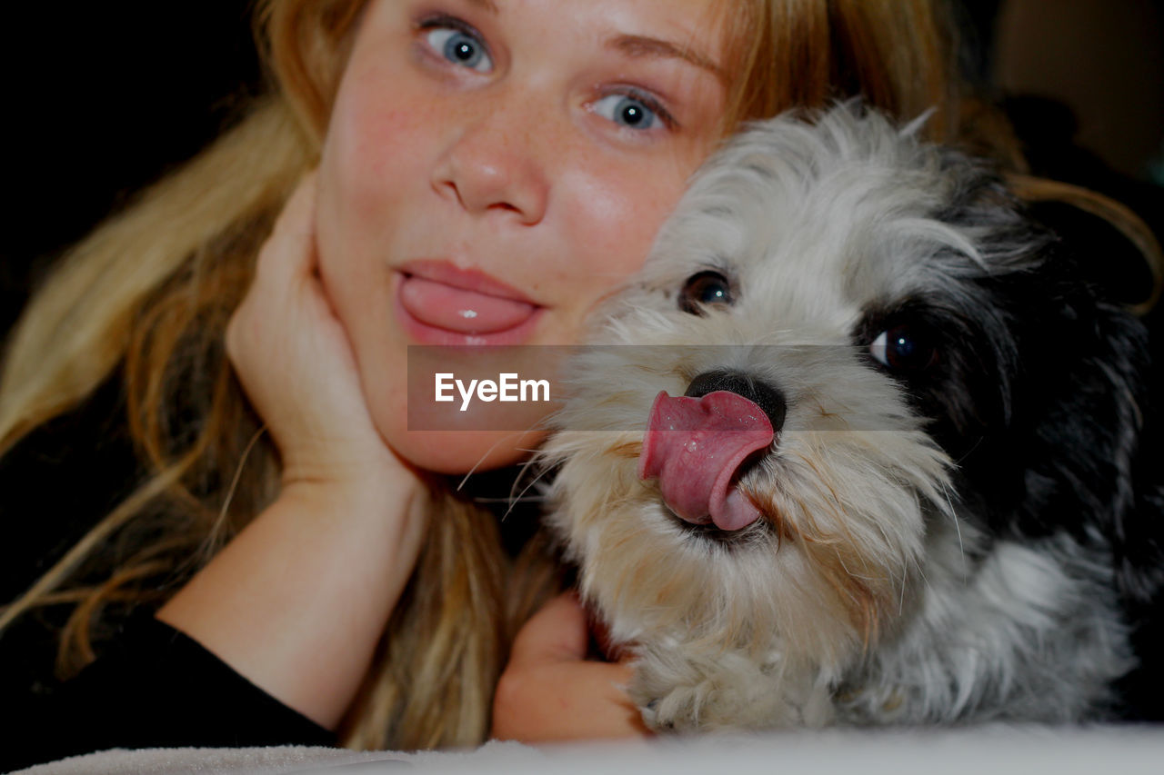 Portrait of young woman and dog sticking out tongue at home