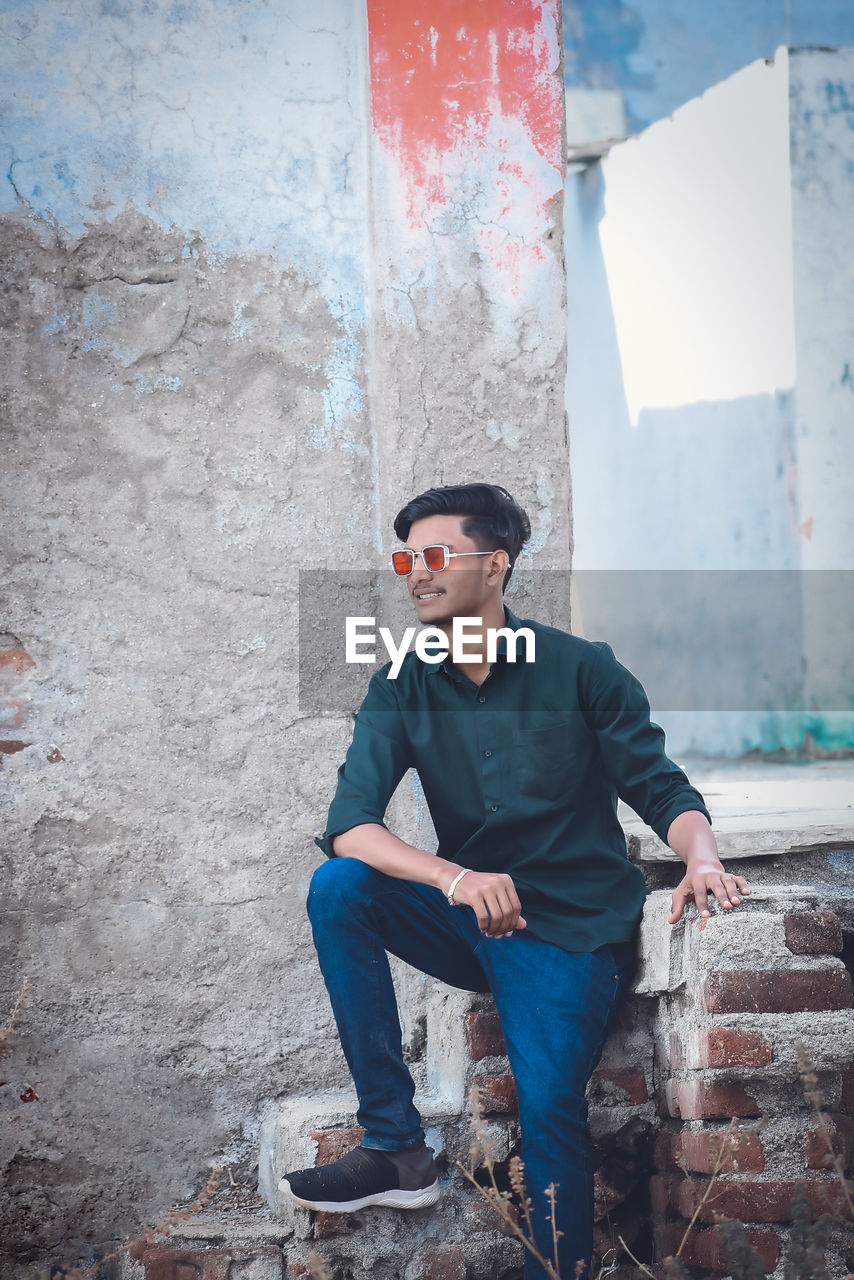 YOUNG MAN LOOKING AT CAMERA AGAINST WALL