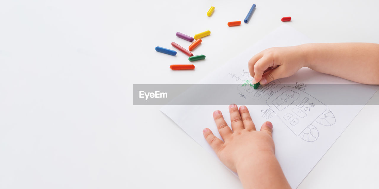 Toddler draws colorful robot with wax crayons. white background with copy space.