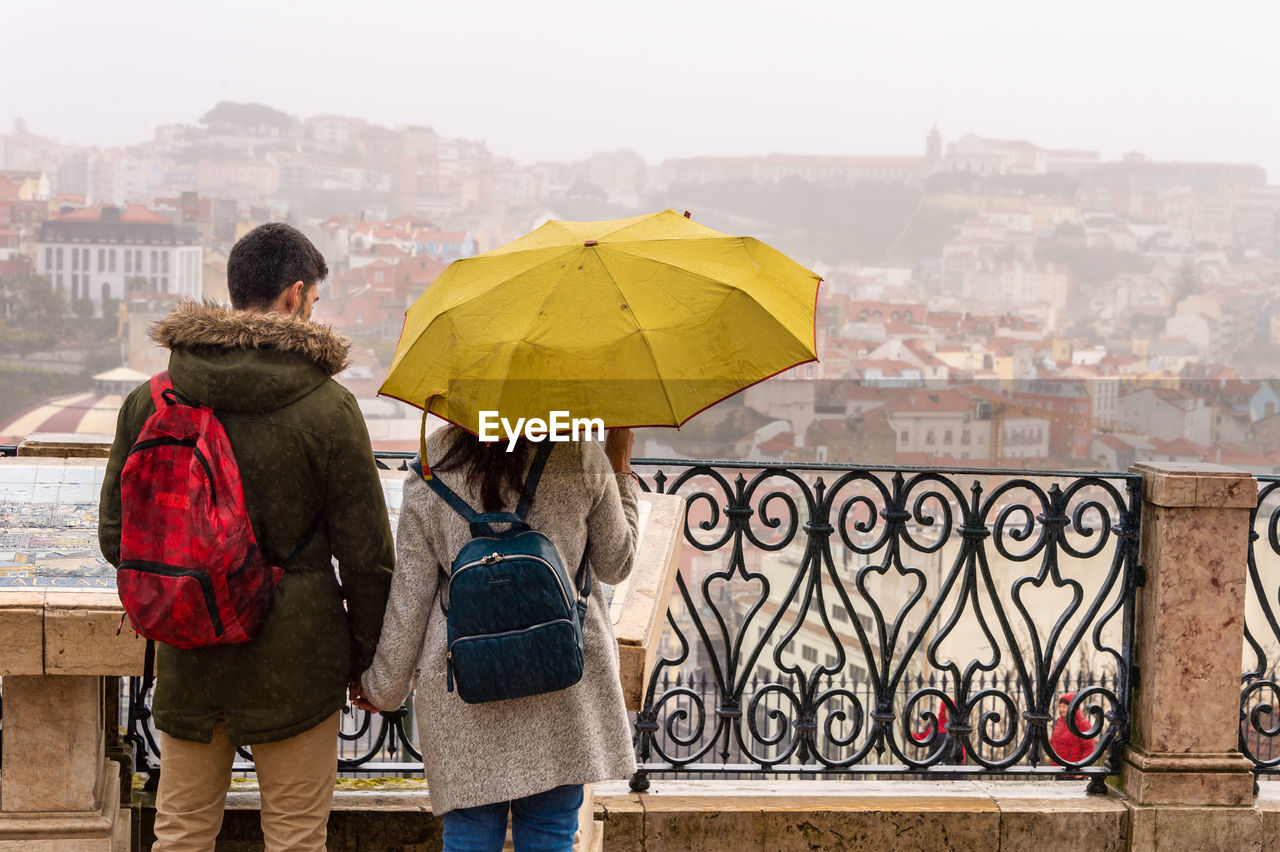 REAR VIEW OF PEOPLE STANDING ON RAILING IN RAIN