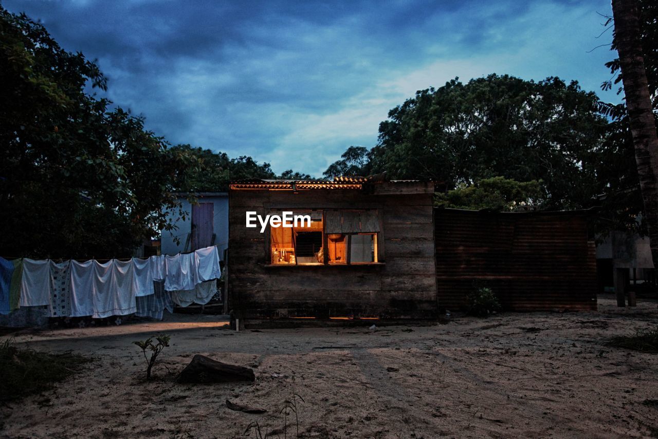 Clothes drying on clothesline by hut against cloudy sky