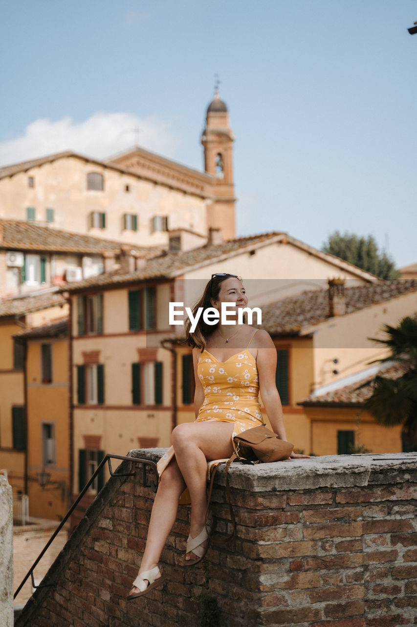 full length of young woman sitting on steps against sky