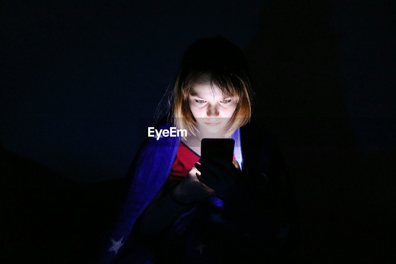 Beautiful woman using mobile phone in darkroom