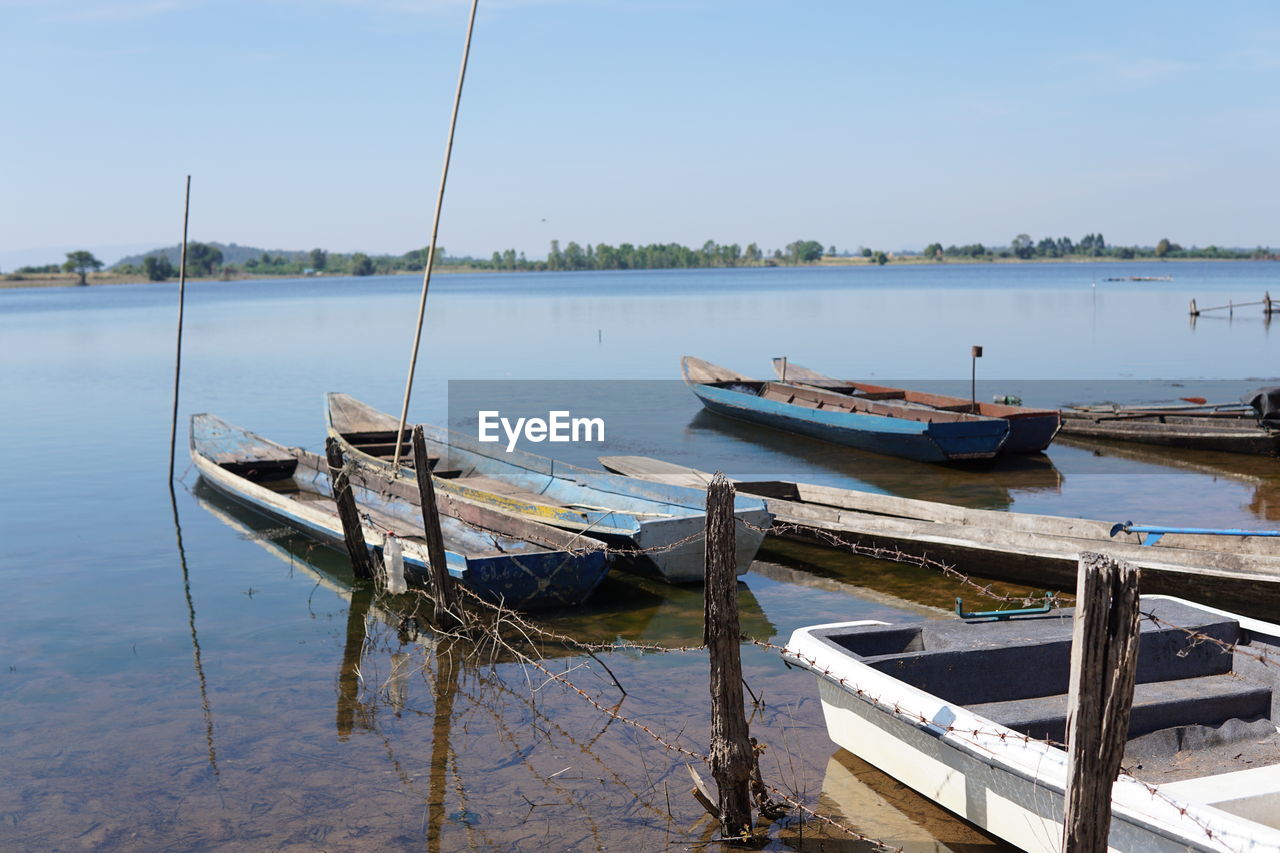 Old rowboats moored in lake against sky