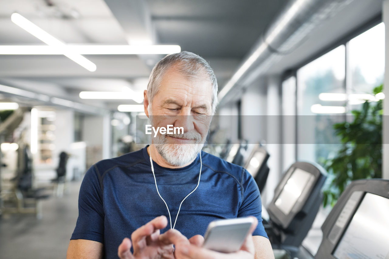 Senior man with smartphone and earphones in gym