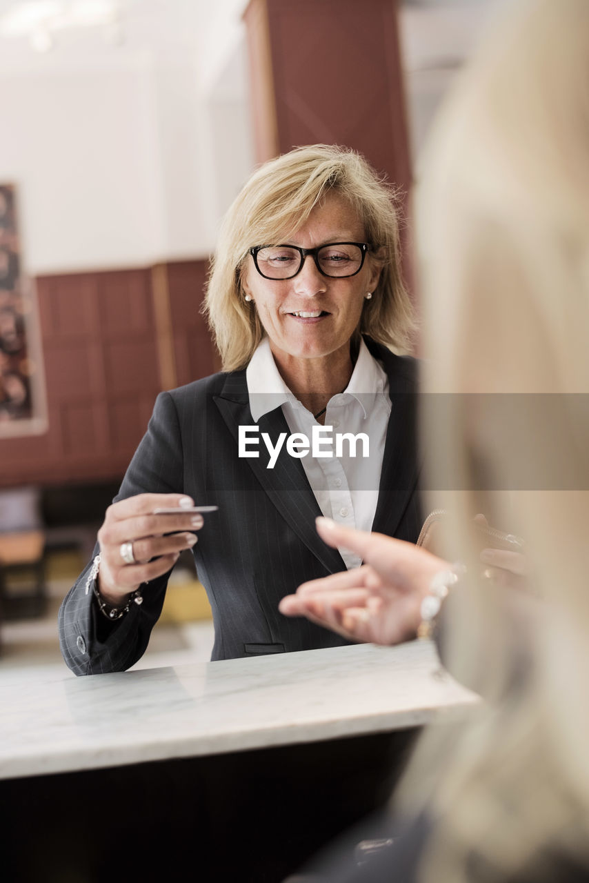 Happy mature businesswoman paying receptionist with credit card at hotel checkout