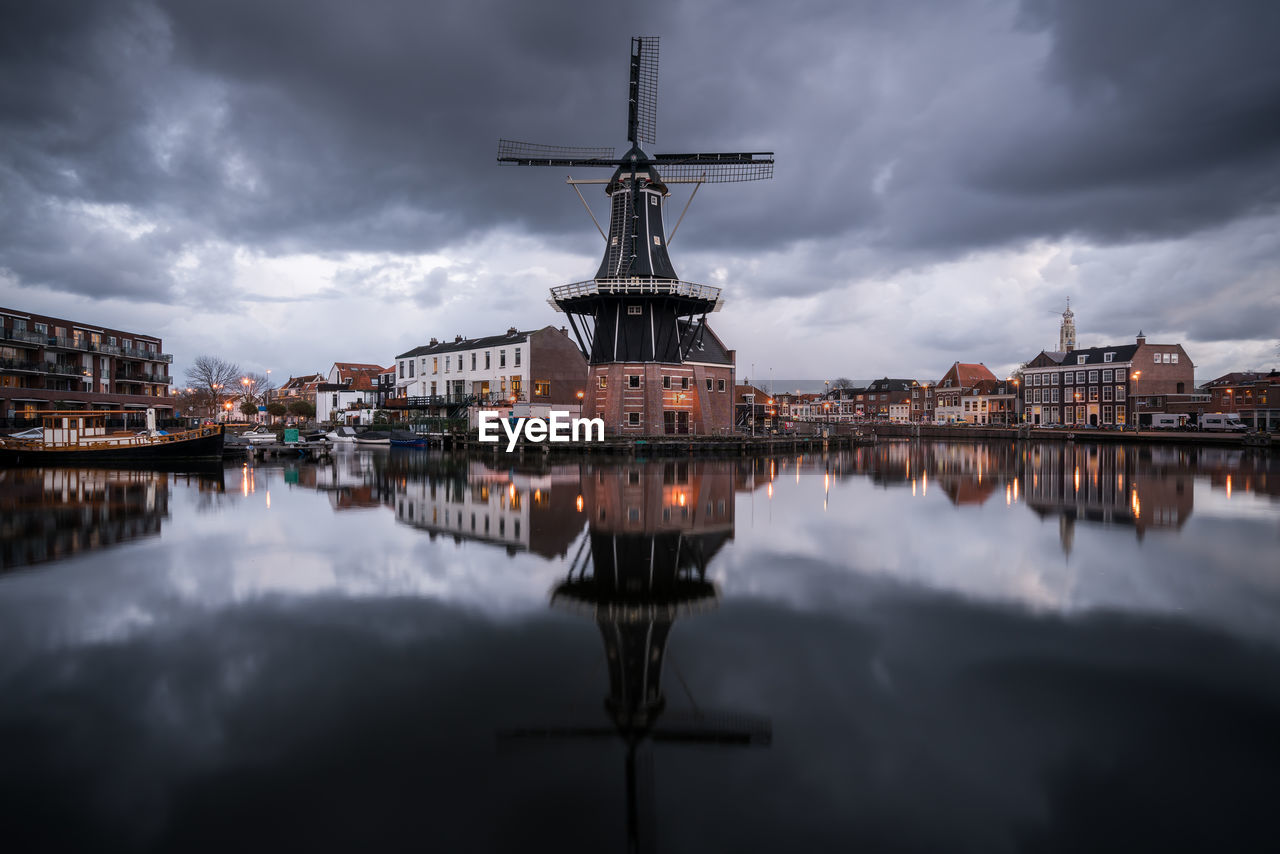 Reflection of traditional windmill on river in city at dusk