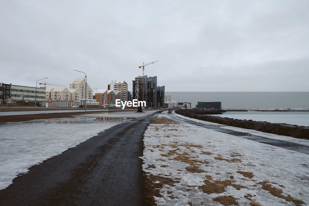 Snow covered buildings by sea against sky