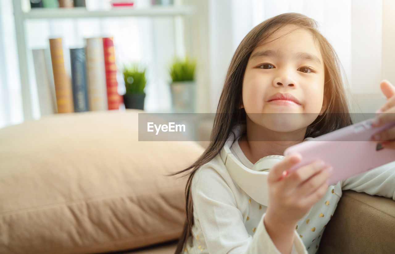 PORTRAIT OF GIRL HOLDING MOBILE AT HOME