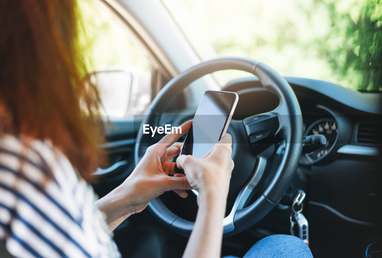 Crop photo of young woman driver using mobile phone in hands sitting in car in summer time